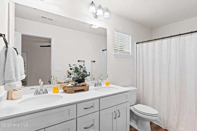 full bath with visible vents, a sink, double vanity, and toilet