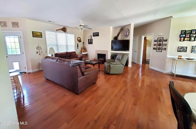 living room with baseboards, light wood finished floors, ceiling fan, and a fireplace