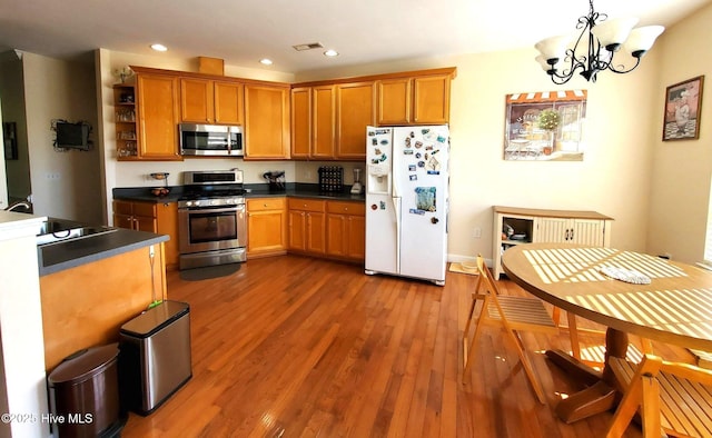 kitchen with wood finished floors, a sink, a chandelier, stainless steel appliances, and recessed lighting