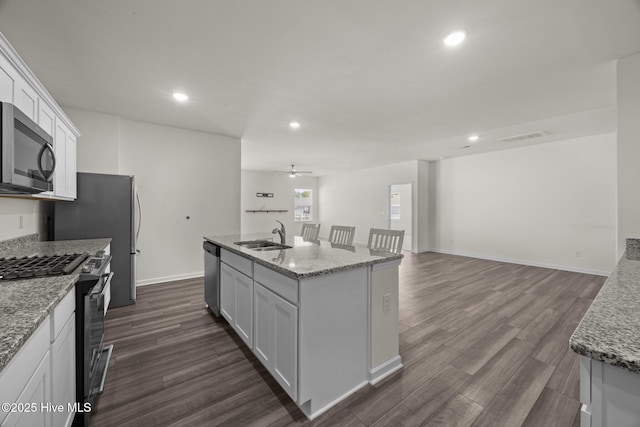 kitchen featuring an island with sink, dark wood-style floors, white cabinets, a sink, and appliances with stainless steel finishes