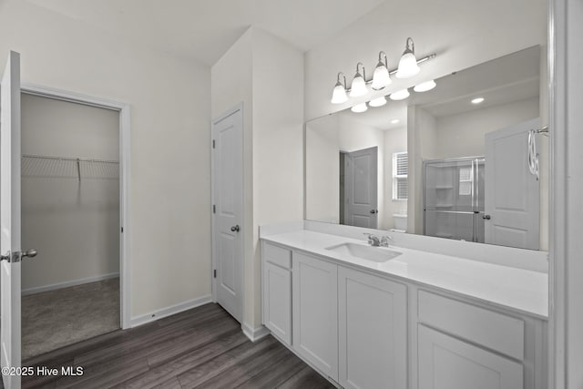 bathroom with a walk in closet, a shower stall, wood finished floors, vanity, and baseboards
