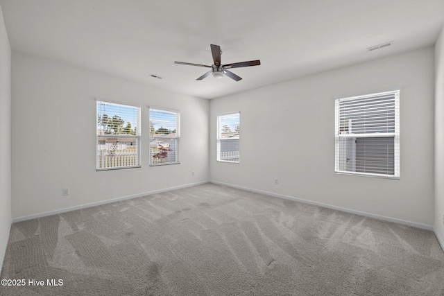 empty room featuring light colored carpet, baseboards, ceiling fan, and a healthy amount of sunlight