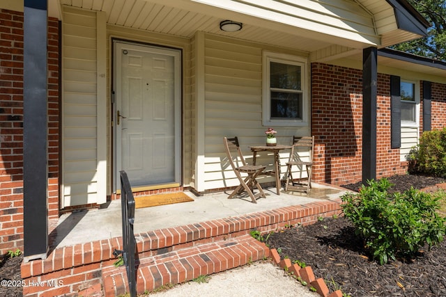 view of exterior entry with brick siding and a porch