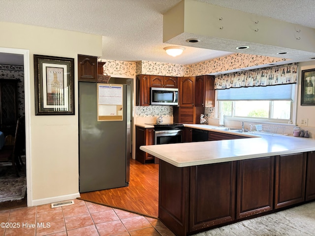 kitchen with a peninsula, a sink, light countertops, appliances with stainless steel finishes, and light tile patterned flooring