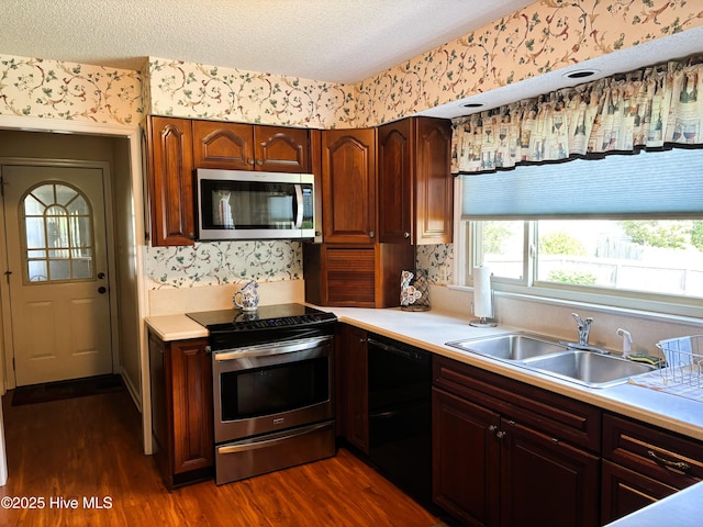 kitchen with a sink, wallpapered walls, stainless steel appliances, dark wood-type flooring, and light countertops