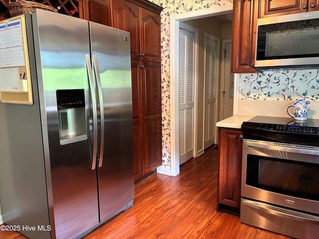 kitchen featuring wood finished floors, light countertops, wallpapered walls, and appliances with stainless steel finishes