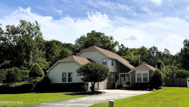 view of front facade featuring concrete driveway, brick siding, fence, and a front yard
