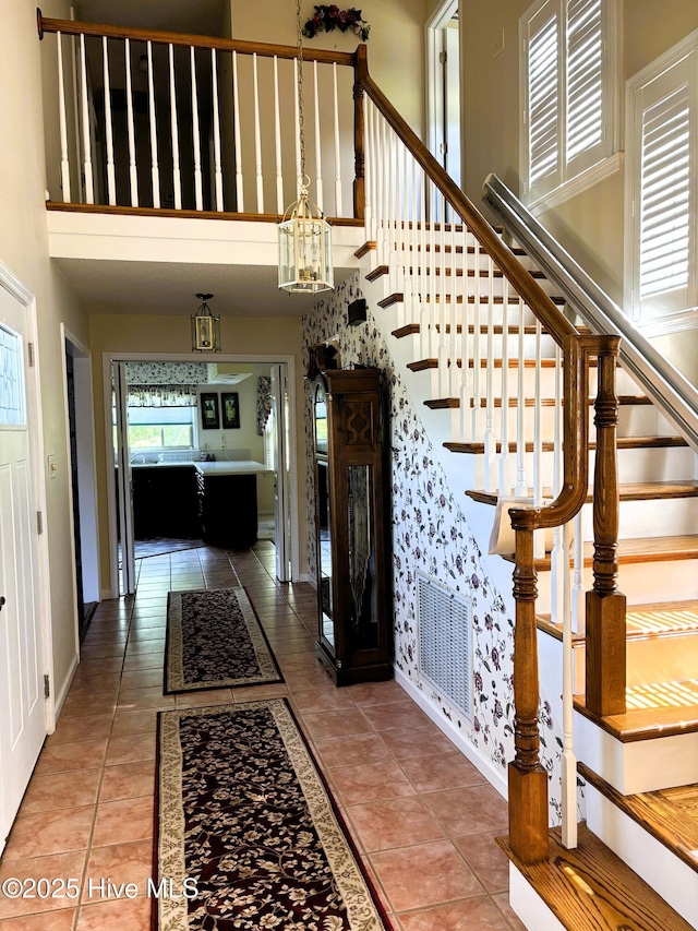 entrance foyer with baseboards, stairs, visible vents, and a high ceiling