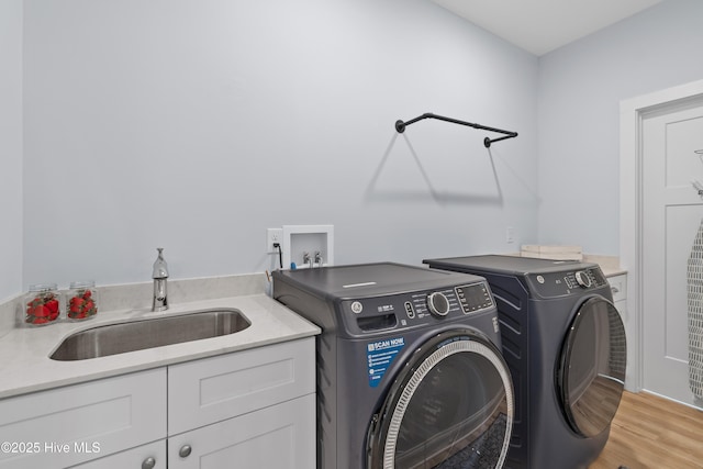 clothes washing area with cabinet space, separate washer and dryer, a sink, and light wood-type flooring