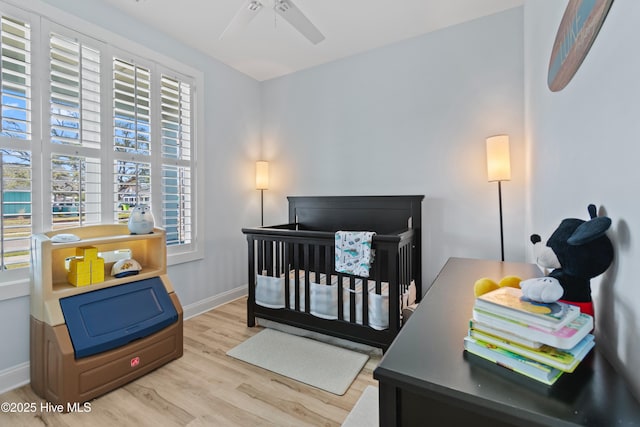 bedroom featuring a nursery area, multiple windows, baseboards, and wood finished floors