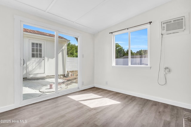 spare room featuring an AC wall unit, baseboards, and wood finished floors