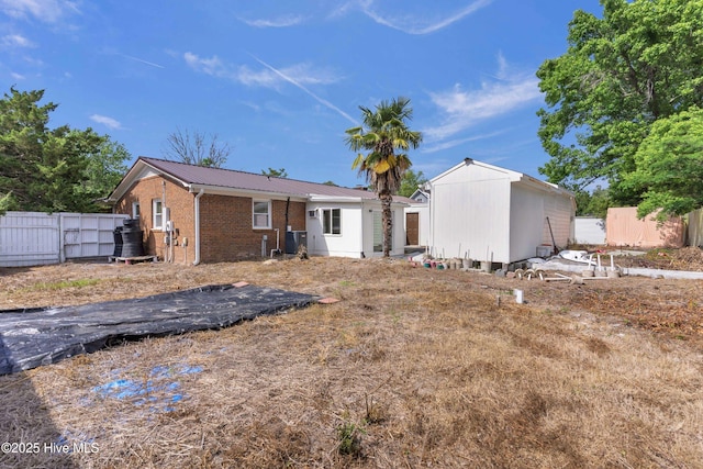 rear view of property featuring brick siding, fence, a shed, and metal roof