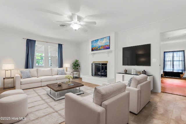 living room featuring visible vents, a ceiling fan, and a glass covered fireplace