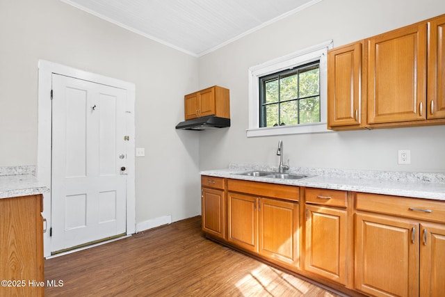 kitchen with brown cabinets, wood finished floors, a sink, light countertops, and ornamental molding