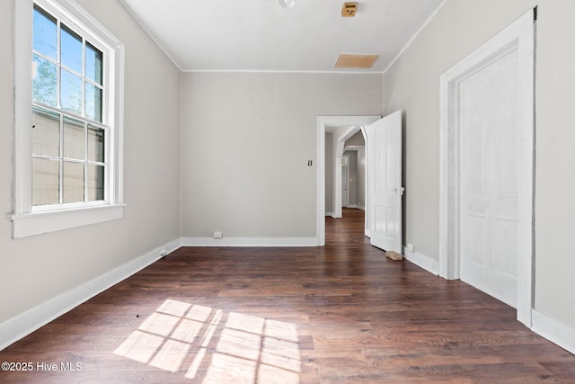 unfurnished bedroom featuring crown molding, baseboards, arched walkways, and wood finished floors