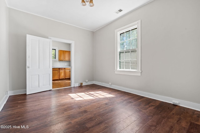 empty room featuring visible vents, dark wood-style flooring, and baseboards