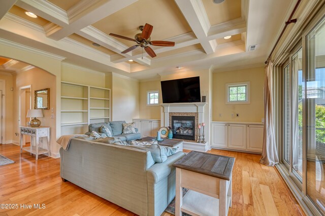 living room featuring crown molding, a glass covered fireplace, a wealth of natural light, and coffered ceiling