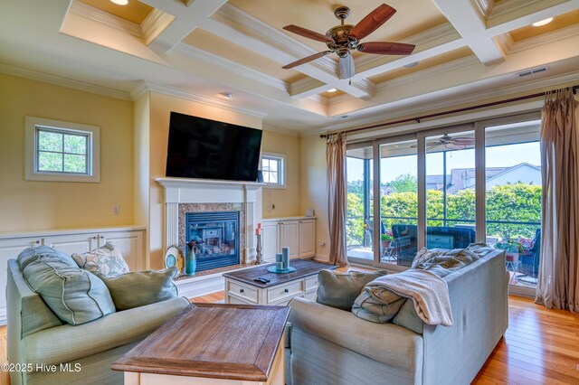 living area featuring ceiling fan, a premium fireplace, beamed ceiling, ornamental molding, and coffered ceiling