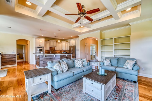 living area with arched walkways, a ceiling fan, ornamental molding, and coffered ceiling