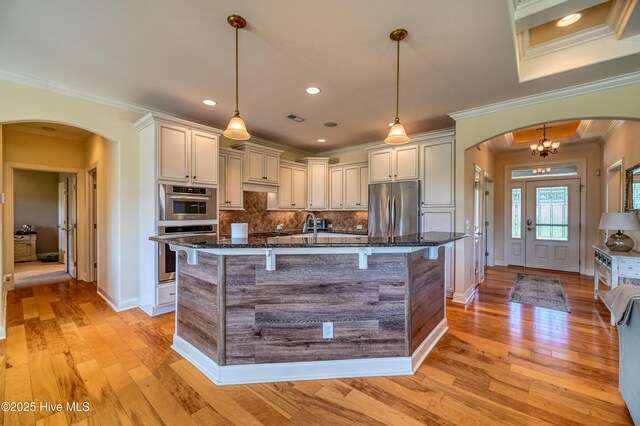 kitchen with a breakfast bar area, arched walkways, dark stone countertops, stainless steel fridge, and ornamental molding