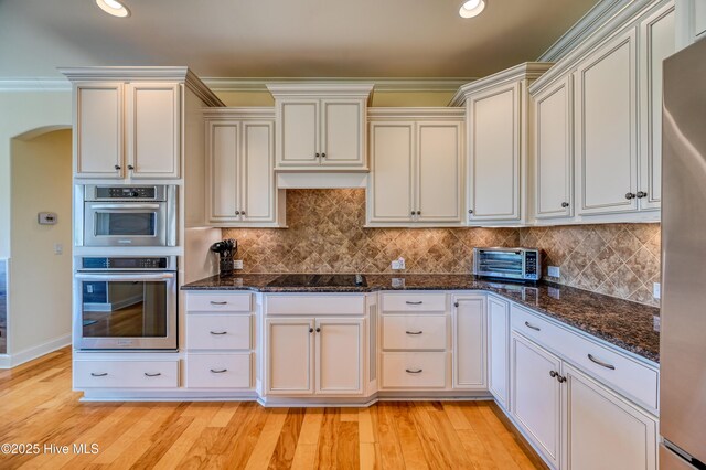 kitchen with a toaster, light wood-style floors, dark stone counters, tasteful backsplash, and stainless steel appliances