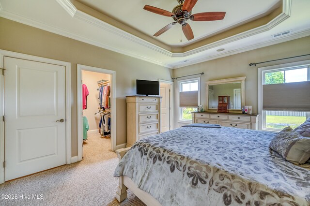 bedroom featuring crown molding, light colored carpet, a walk in closet, a tray ceiling, and visible vents
