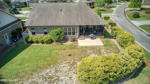 rear view of property featuring a lawn, brick siding, a sunroom, and roof with shingles