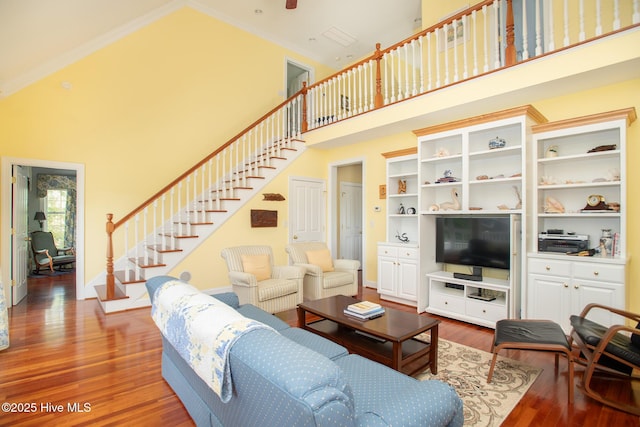 living area with high vaulted ceiling, stairs, baseboards, wood finished floors, and ornamental molding