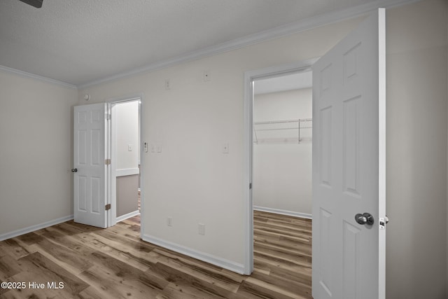 unfurnished bedroom featuring a closet, ornamental molding, wood finished floors, baseboards, and a spacious closet