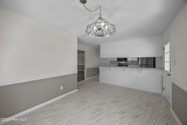 kitchen with a notable chandelier, a breakfast bar area, freestanding refrigerator, a peninsula, and decorative backsplash