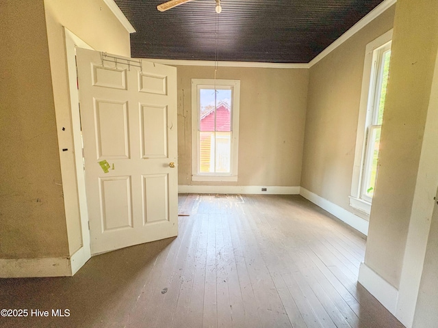 empty room with crown molding, baseboards, plenty of natural light, and wood-type flooring