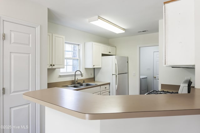 kitchen with a sink, freestanding refrigerator, a peninsula, white cabinetry, and visible vents