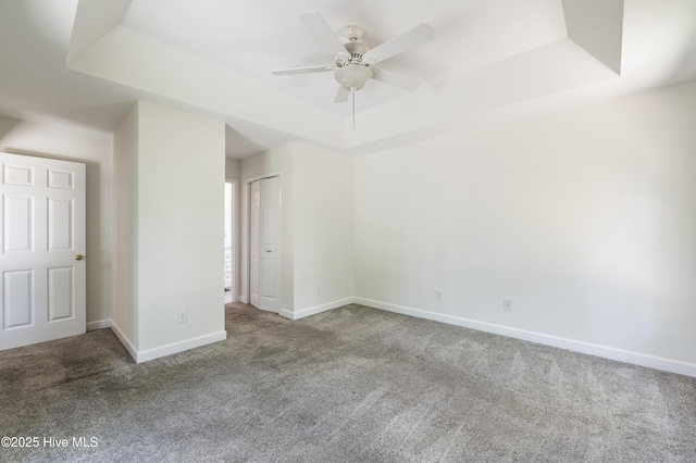 carpeted spare room featuring baseboards, a tray ceiling, and ceiling fan