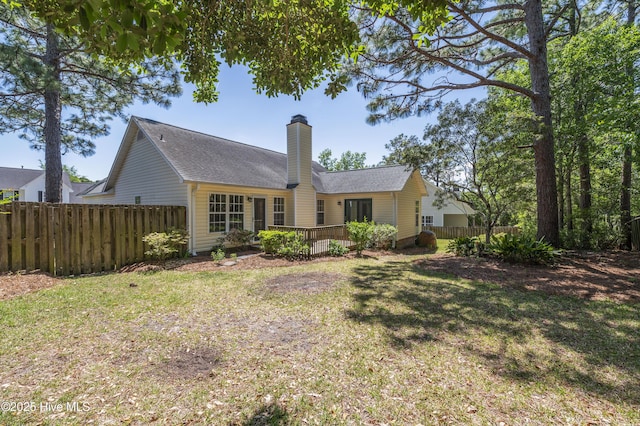 rear view of house featuring a wooden deck, fence, roof with shingles, a chimney, and a yard