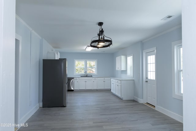 kitchen featuring crown molding, white cabinets, a sink, freestanding refrigerator, and visible vents