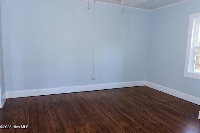 empty room featuring baseboards, ornamental molding, and dark wood-type flooring