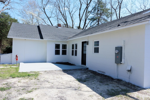 exterior space with concrete block siding, a patio, a chimney, and roof with shingles