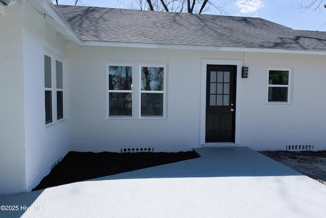 entrance to property with concrete block siding, a shingled roof, and crawl space