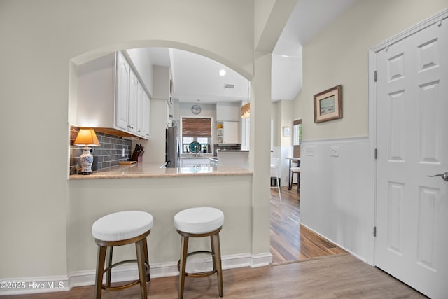 1710 Deerfield Ct SW Unit 4A, Ocean Isle Beach, NC 28469 - kitchen featuring freestanding refrigerator, white cabinets, wood finished floors, arched walkways, and a kitchen bar