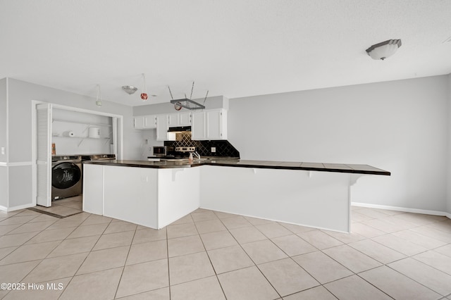 2910 Mulberry Ln Unit B, Greenville, NC 27858 - kitchen featuring washer / dryer, a peninsula, dark countertops, white cabinetry, and tasteful backsplash