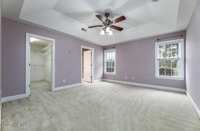 unfurnished bedroom featuring multiple windows, a tray ceiling, and light carpet