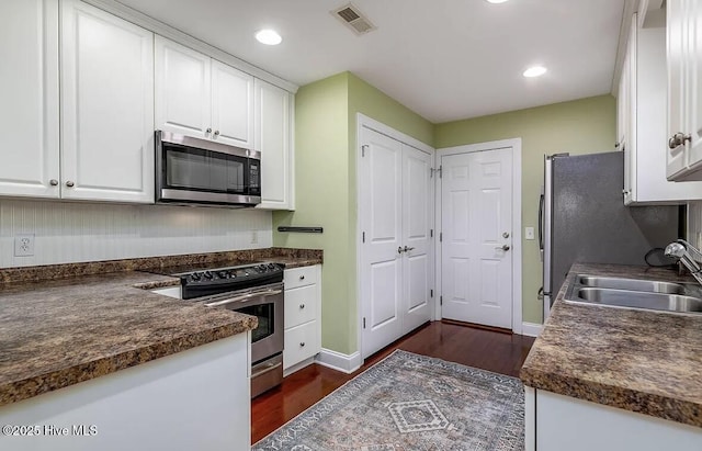 kitchen featuring white cabinets, dark countertops, appliances with stainless steel finishes, a sink, and visible vents