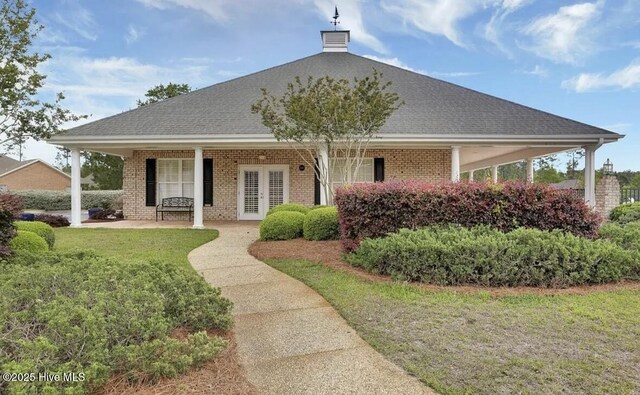 exterior space featuring a shingled roof, brick siding, a porch, a front yard, and french doors