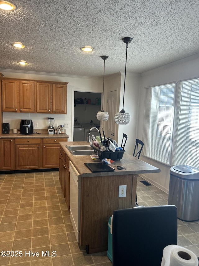 kitchen featuring light tile patterned flooring, brown cabinets, a sink, independent washer and dryer, and dishwasher