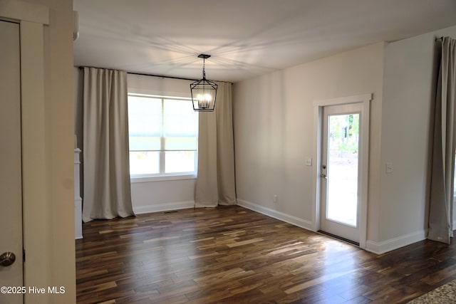 unfurnished dining area with a healthy amount of sunlight, baseboards, an inviting chandelier, and dark wood finished floors