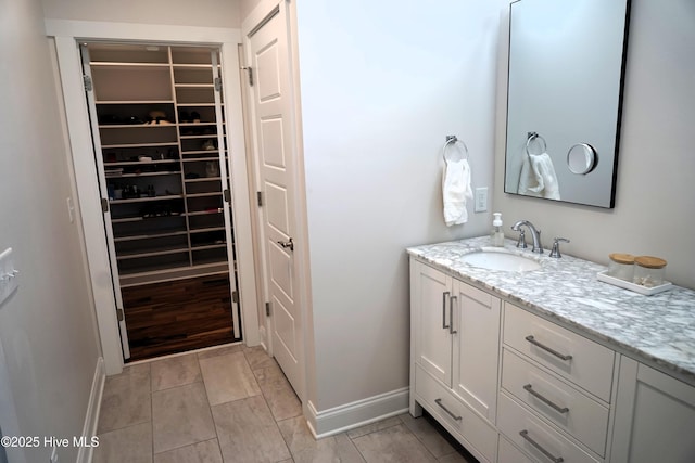 bathroom featuring baseboards, a walk in closet, and vanity