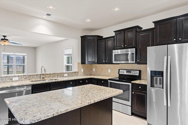 kitchen with appliances with stainless steel finishes, a sink, a center island, tasteful backsplash, and visible vents