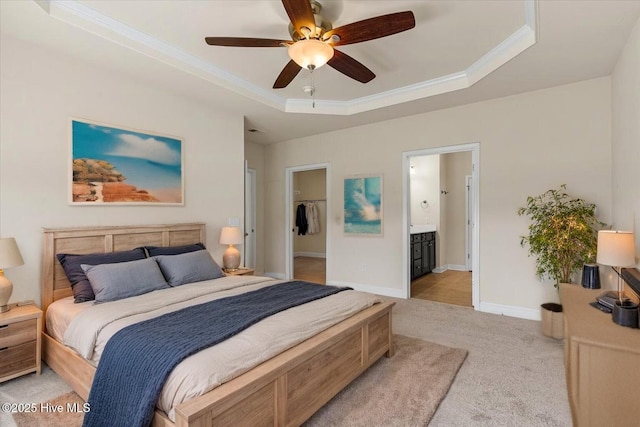 bedroom with a walk in closet, light colored carpet, a raised ceiling, ornamental molding, and ensuite bathroom