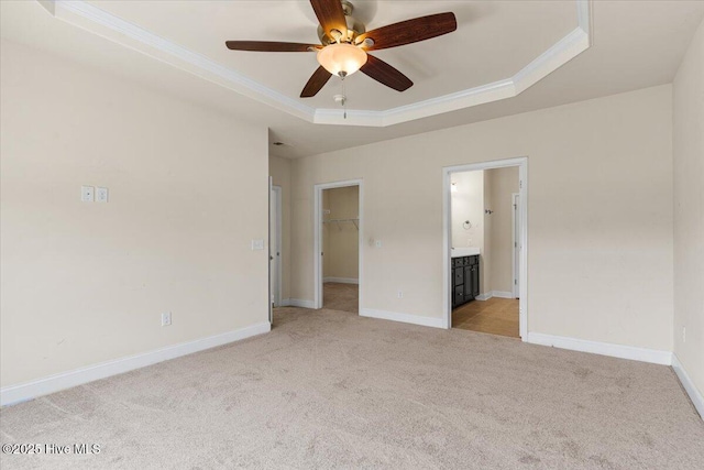unfurnished bedroom featuring ornamental molding, light carpet, baseboards, a raised ceiling, and a spacious closet