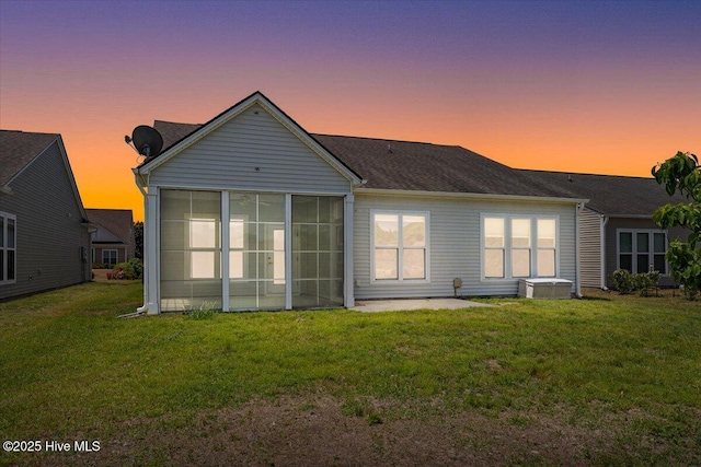 back of house at dusk featuring a lawn and a sunroom